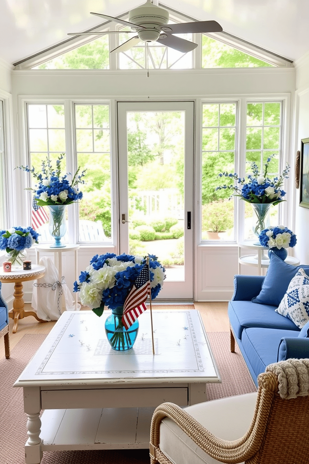 A bright sunroom filled with natural light features a large window that opens to a beautiful garden. The space is adorned with blue and white floral arrangements in elegant vases, creating a fresh and festive atmosphere for Independence Day celebrations. Comfortable seating in shades of blue complements the decor, while a whitewashed coffee table holds a small American flag centerpiece. The sunroom's walls are decorated with patriotic art, enhancing the cheerful ambiance of the space.