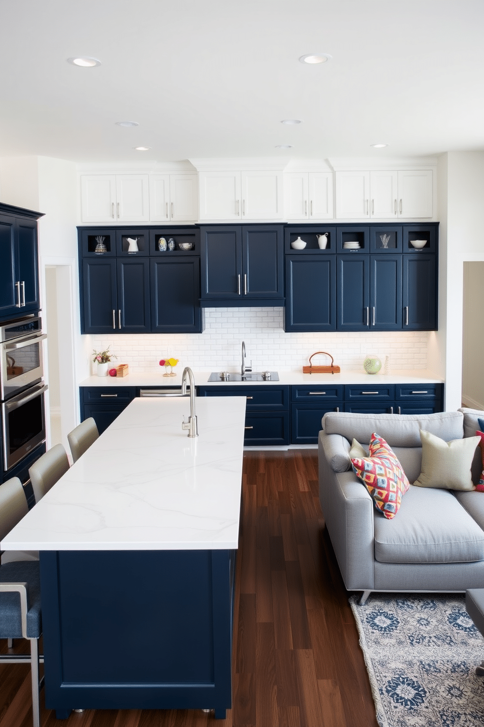 A spacious kitchen family room combo featuring contrasting cabinetry for visual interest. The lower cabinets are a deep navy blue, while the upper cabinets are a crisp white, creating a striking balance in the space. In the center, a large kitchen island with a waterfall countertop serves as a focal point, surrounded by stylish bar stools. The family room area includes a comfortable sectional sofa in a soft gray fabric, complemented by colorful throw pillows that tie the room together.