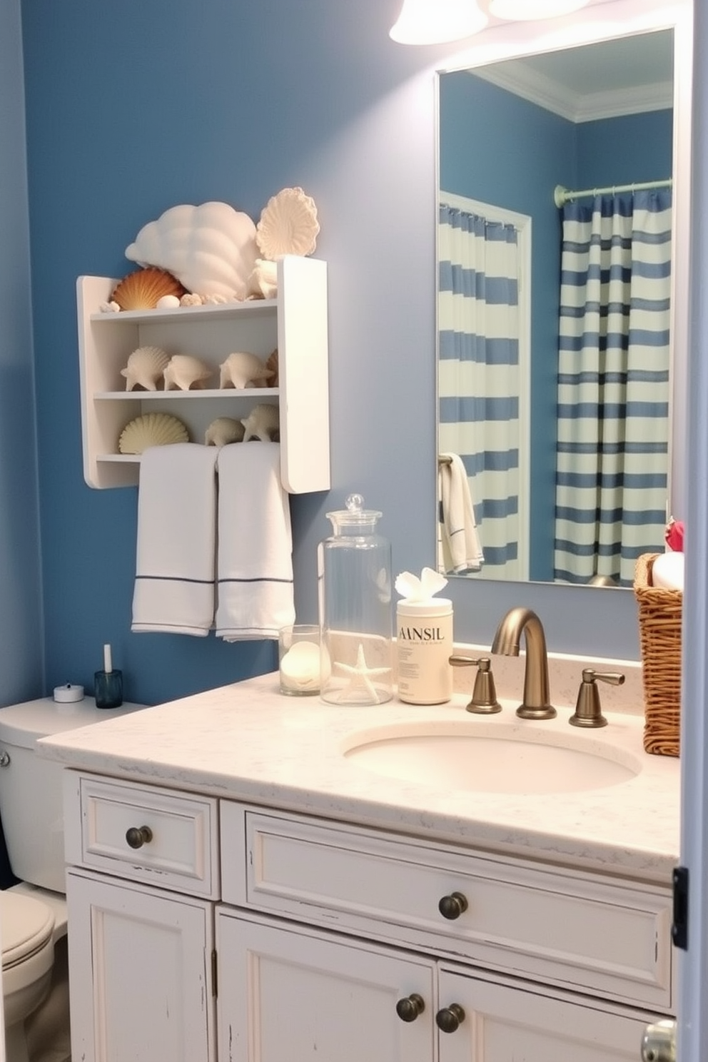 A coastal-themed bathroom featuring seashell accents. The walls are painted in soft blue, and decorative seashells are arranged along the countertop and in a glass jar on the shelf. The vanity has a weathered white finish with a quartz countertop. Nautical-inspired accessories, such as a striped shower curtain and a woven basket, complete the look.