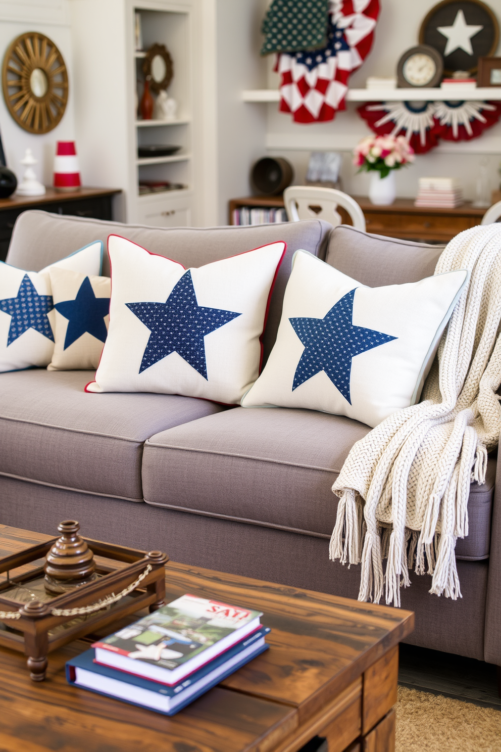 Create a cozy living room setting featuring decorative pillows with star patterns. The pillows are arranged on a plush gray sofa, complemented by a soft knit throw blanket draped casually over one arm. In the background, a festive Labor Day theme is evident with red, white, and blue accents throughout the room. A rustic coffee table holds a small centerpiece of seasonal flowers and a stack of books, enhancing the inviting atmosphere.