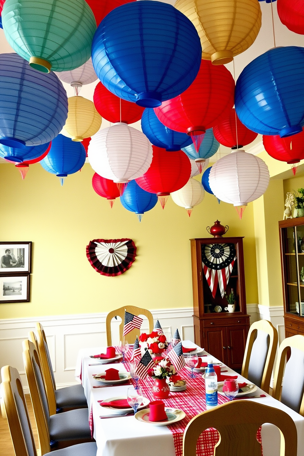 A whimsical dining room setting featuring colorful paper lanterns hanging from the ceiling. The table is set with a festive Labor Day theme, showcasing red, white, and blue decorations and centerpieces.