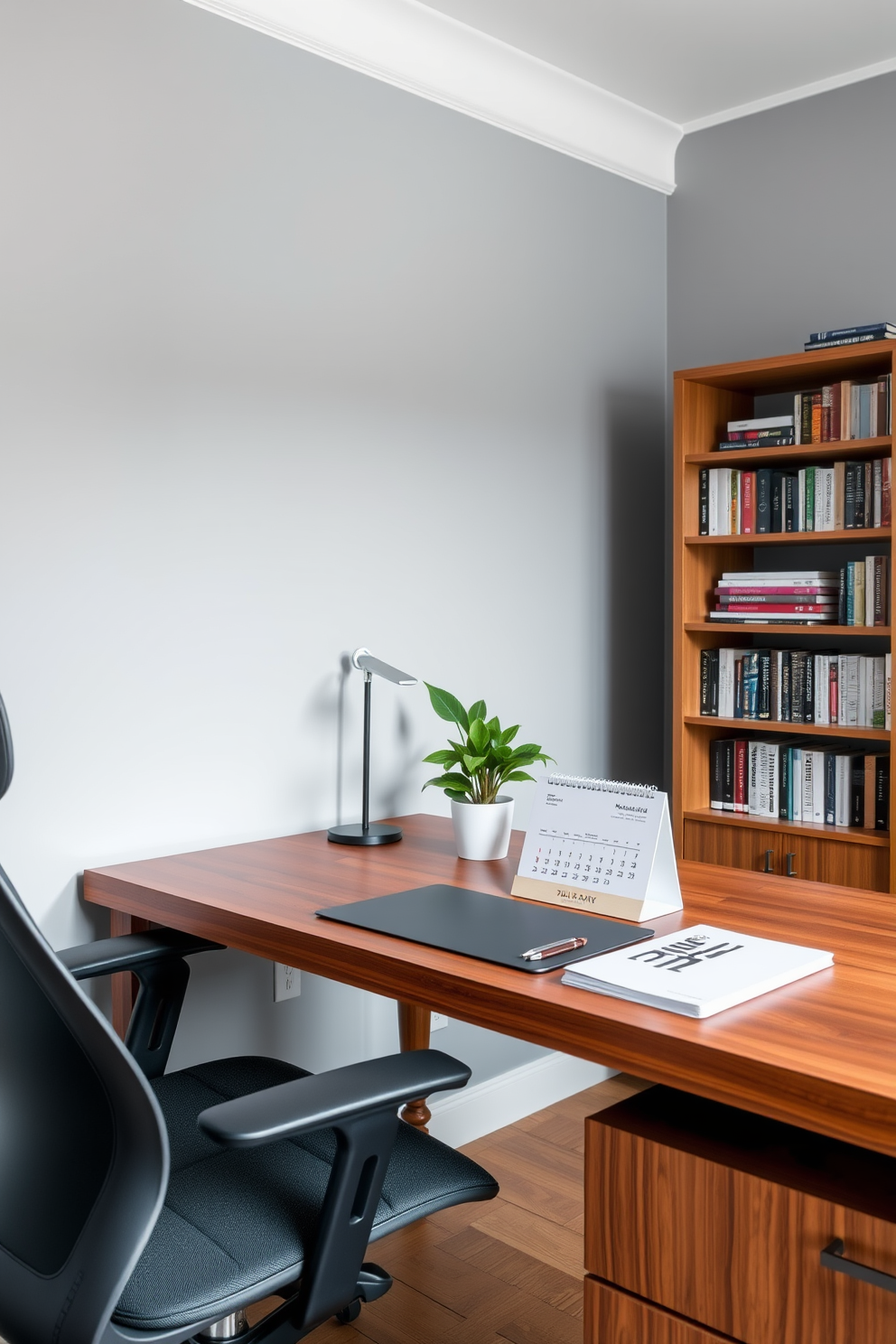 A modern home office space featuring a sleek wooden desk with a stylish desk calendar prominently displayed. The walls are painted in a soft gray tone, and a comfortable ergonomic chair complements the workspace. To the side, a tall bookshelf filled with neatly arranged books adds character to the room. A potted plant sits on the desk, bringing a touch of greenery and life to the decor.