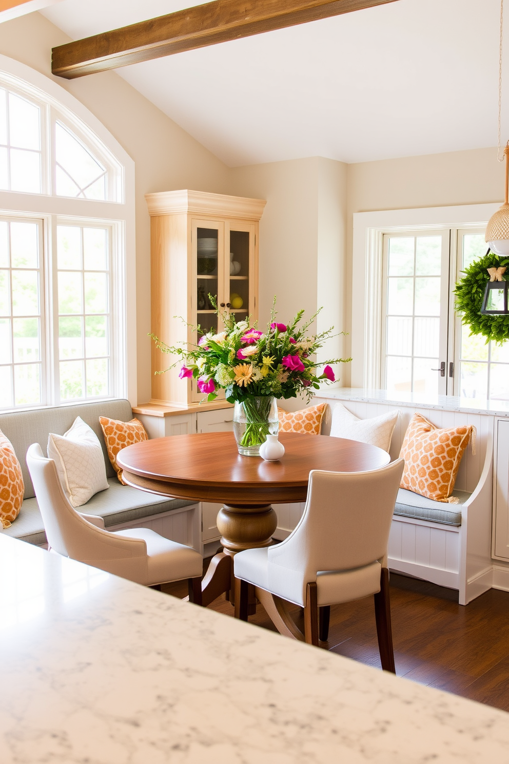 A cozy breakfast nook area featuring a round wooden table surrounded by upholstered chairs in soft pastel colors. Large windows allow natural light to flood the space, while a built-in bench with cushions adds comfort and charm. Labor Day kitchen decorating ideas include a festive display of fresh flowers in a vibrant vase on the countertop. Hang string lights above the island to create a warm and inviting atmosphere for gatherings.