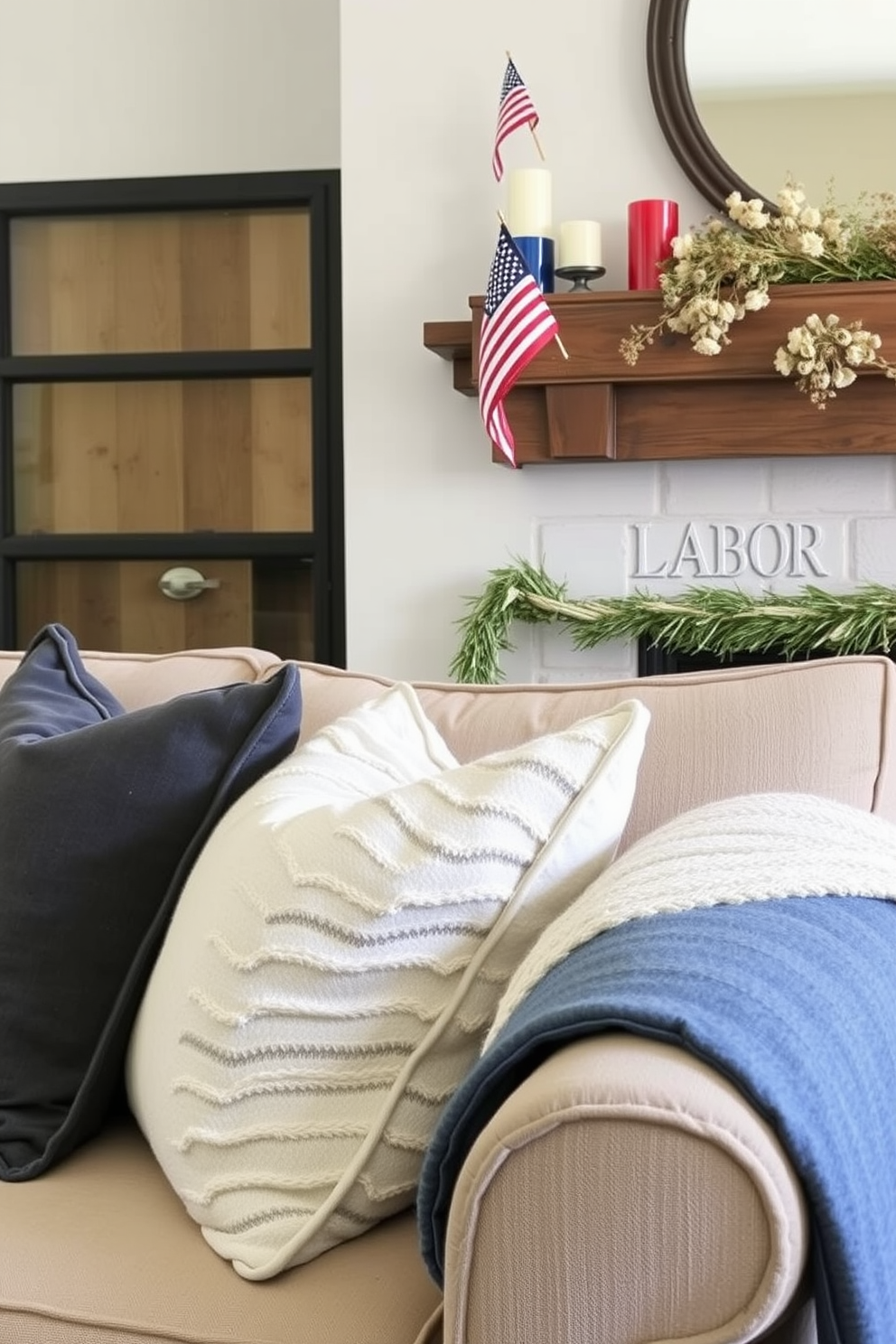 Layered textiles create a cozy living room atmosphere. Plush throw pillows of varying sizes and textures are arranged on a deep-seated sofa, complemented by a soft, woven blanket draped over the arm. For Labor Day mantel decorating, a rustic wooden mantel serves as the backdrop. Seasonal accents like small American flags, red and blue candles, and a garland of dried flowers bring a festive touch to the space.