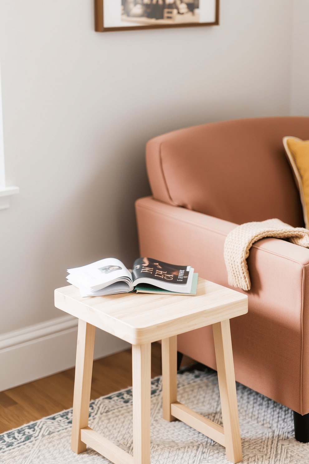 A cozy reading nook featuring a small side table designed for drinks and snacks. The table is made of light wood with a smooth finish and has a minimalist design that complements the surrounding decor. Next to the table, a plush armchair upholstered in soft fabric invites relaxation. A warm throw blanket is draped over the armrest, and a stack of books rests on the table, ready for leisurely reading.