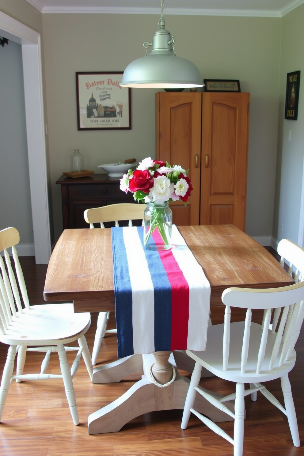 A charming dining area featuring a red white and blue table runner elegantly draped across a rustic wooden table. Surrounding the table are mismatched chairs that add a touch of eclectic charm to the small space. On the table, a centerpiece of fresh flowers in a mason jar complements the patriotic colors of the runner. Soft lighting from a nearby pendant lamp creates a warm and inviting atmosphere, perfect for a Labor Day gathering.