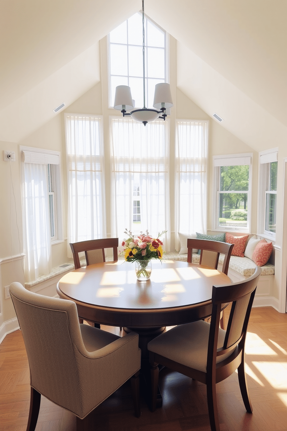 A sun-drenched breakfast area features a large round wooden table surrounded by comfortable upholstered chairs. Sunlight streams through expansive windows adorned with sheer white curtains, illuminating a fresh vase of seasonal flowers at the center of the table. The walls are painted in a soft pastel hue, creating a warm and inviting atmosphere. A cozy nook with built-in benches and colorful cushions invites relaxation and conversation, making it the perfect spot for morning coffee.