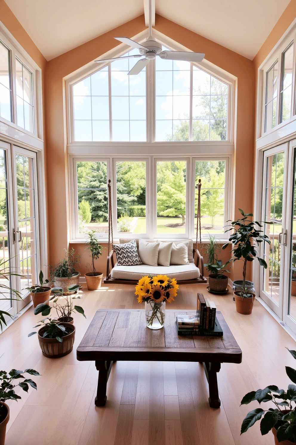 A bright sunroom filled with natural light features large windows that open to a beautiful garden view. In the center, a cozy seating area includes a swing chair suspended from the ceiling, adorned with soft cushions for comfort. The walls are painted in a warm beige tone, and the floor is covered with a light-colored wood. Potted plants are scattered throughout the space, and a rustic wooden coffee table sits in front of the swing chair, topped with a few decorative books and a fresh bouquet of sunflowers.