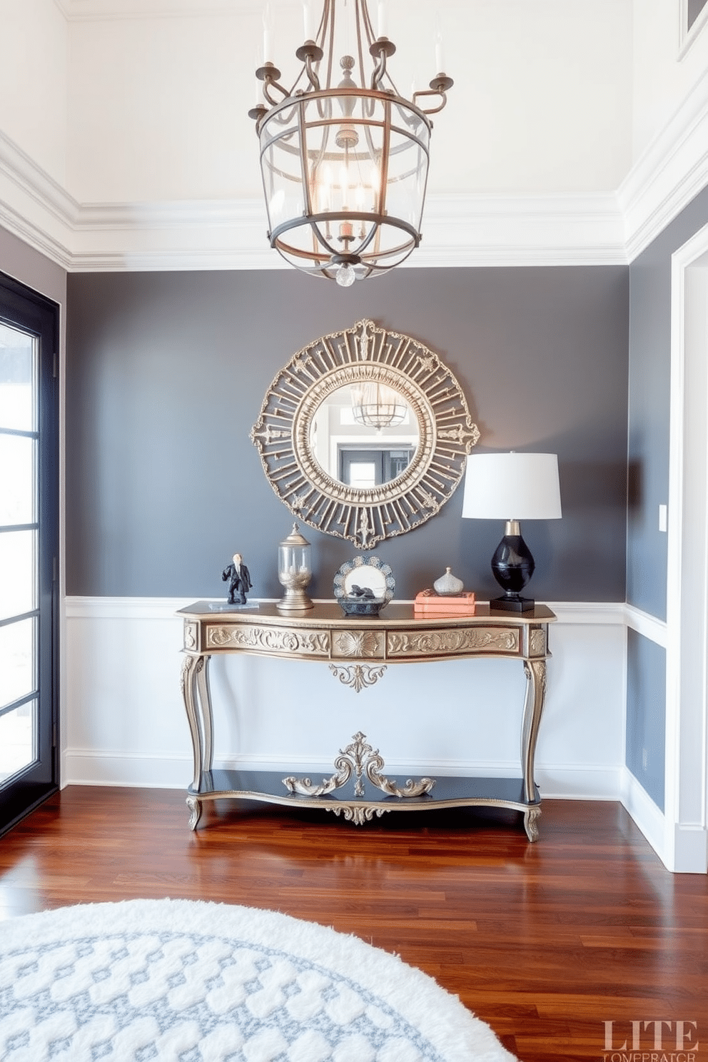 An elegant console table is positioned against the wall, adorned with a decorative mirror that reflects natural light. The table features intricate detailing and is complemented by a stylish lamp and a curated selection of decorative objects. The entryway is spacious and inviting, with a statement chandelier hanging from the ceiling. Rich hardwood floors lead to a plush area rug, adding warmth and texture to the sophisticated design.