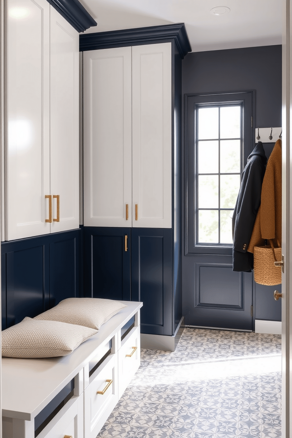 A stylish laundry mudroom featuring two-tone cabinetry that combines a deep navy blue lower section with crisp white upper cabinets. The cabinetry is accented with brushed gold hardware, providing a modern touch while offering ample storage for laundry essentials and outdoor gear. The space includes a built-in bench with plush cushions, perfect for putting on shoes, and a decorative wall rack for hanging coats and bags. A patterned tile floor adds texture and visual interest, while a large window allows natural light to flood the room, creating an inviting atmosphere.