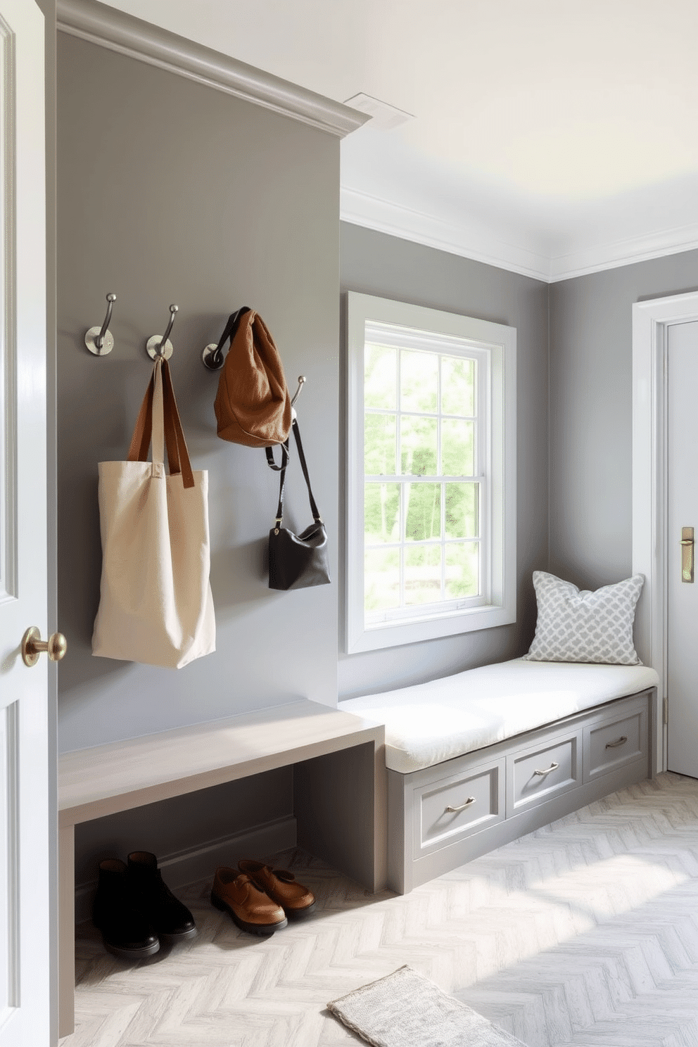 A stylish mudroom features a row of elegant hooks made from brushed nickel, perfect for hanging coats and bags. The walls are painted in a soft gray, complemented by a durable tile floor in a herringbone pattern. Adjacent to the hooks, a built-in bench with plush cushions provides a cozy spot for putting on shoes. Natural light floods the space through a large window, enhancing the inviting atmosphere of this functional laundry mudroom design.