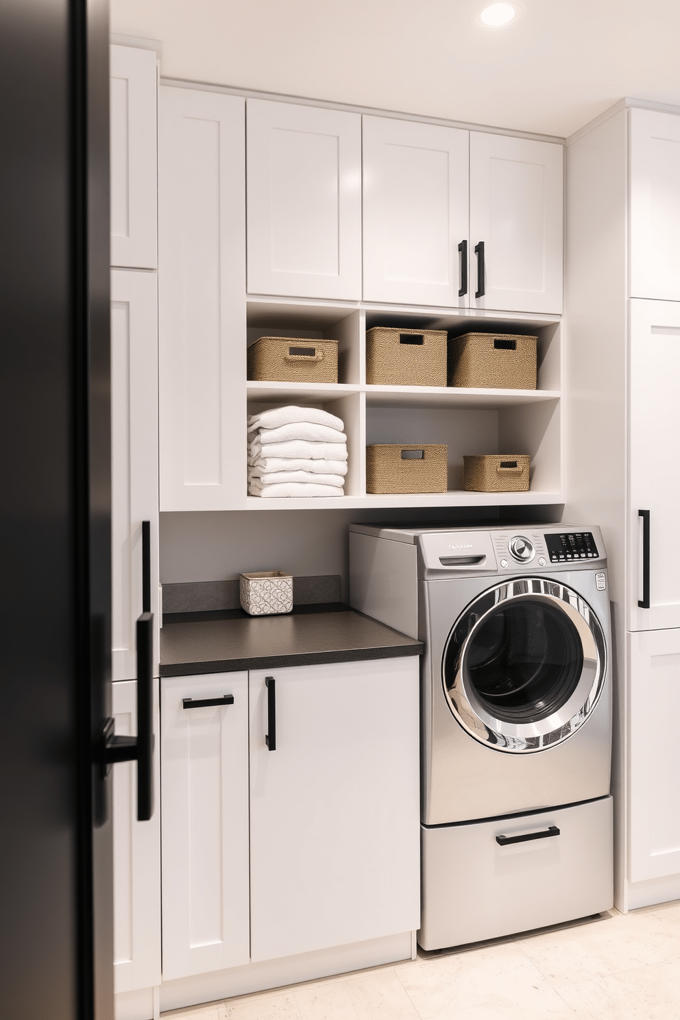 A modern laundry room featuring modular cabinets that allow for customizable storage solutions. The cabinets are finished in a sleek white with contrasting matte black hardware, providing a clean and contemporary look. The space includes a designated area for a washer and dryer, seamlessly integrated into the cabinetry. Above the appliances, open shelving displays neatly folded towels and decorative storage bins for a functional yet stylish design.