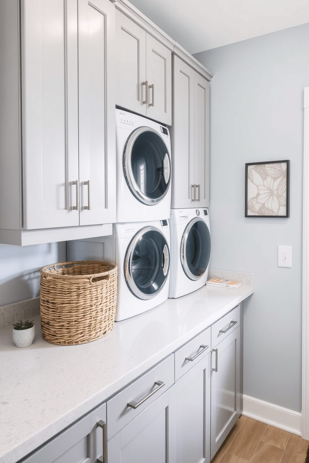 A modern laundry room featuring a stacked washer and dryer setup. The cabinetry is a soft gray, complementing the white appliances, while the walls are painted in a light blue hue for a refreshing vibe. The countertop is a sleek quartz surface in a subtle veining pattern, providing ample space for folding clothes. A stylish laundry basket in woven natural fibers adds warmth, and a small potted plant sits on the countertop for a touch of greenery.