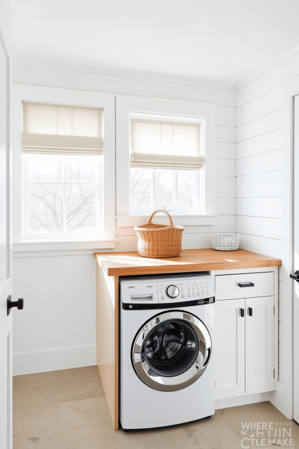 A modern farmhouse laundry room features shiplap walls painted in a soft white hue, creating a bright and airy atmosphere. The space includes a top-loading washer seamlessly integrated into a custom wooden cabinetry that offers ample storage for laundry essentials. Natural light floods the room through a large window adorned with simple linen curtains, enhancing the farmhouse charm. A rustic wooden countertop sits above the washer, providing a functional space for folding clothes, while a woven basket adds a touch of warmth and texture.