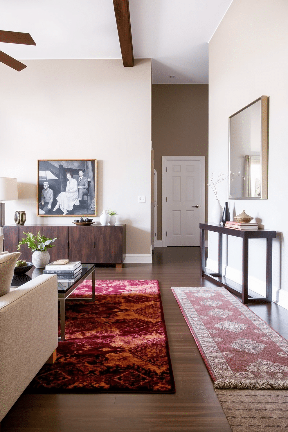 A stylish area rug in rich, deep colors anchors the living room, featuring intricate patterns that complement the surrounding furniture. The rug is placed beneath a modern coffee table, with plush seating arranged around it to create a cozy conversation area. In the entryway, a sleek console table stands against the wall, adorned with decorative accents and a large mirror above it. The floor is adorned with a complementary runner, enhancing the space's warmth and inviting atmosphere.