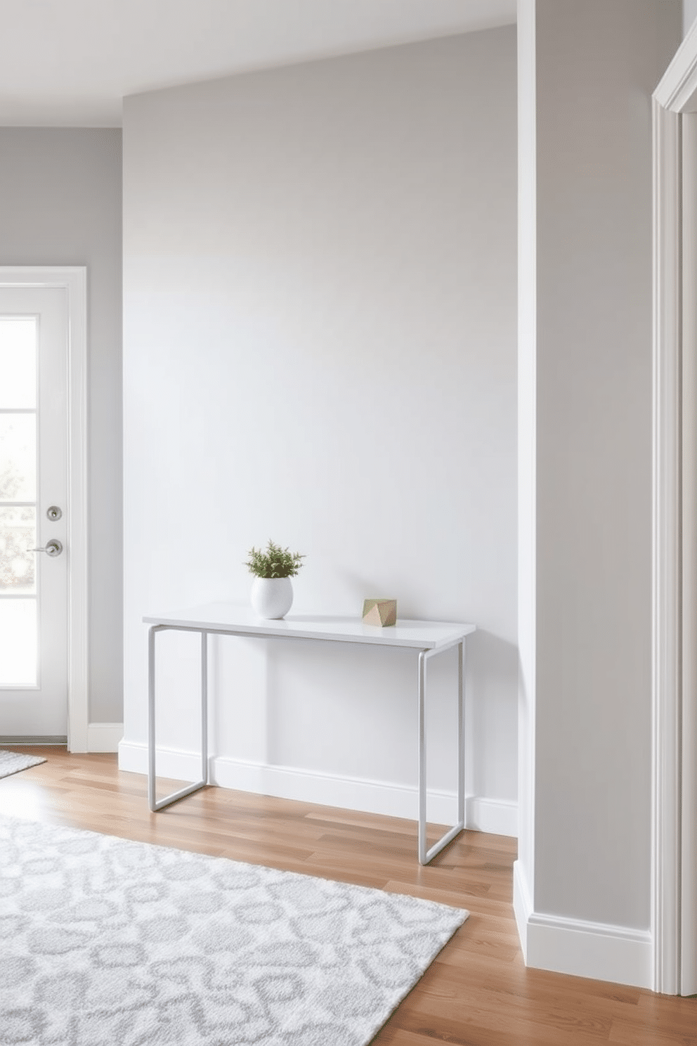 A minimalist console table is positioned against a light gray wall, featuring clean lines and a sleek finish. On the table, a few carefully curated decor accents, including a small potted plant and a geometric sculpture, create an inviting focal point. The entryway is designed with a soft, neutral color palette, complemented by a stylish area rug that adds warmth. Natural light floods the space through a nearby window, enhancing the airy feel and highlighting the simplicity of the decor.