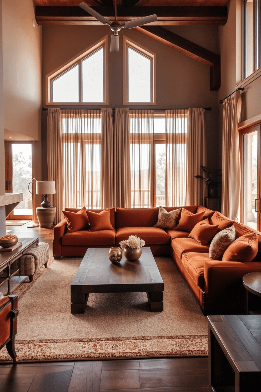 A luxurious family room featuring warm earth tones that create a welcoming atmosphere. The space includes a plush sectional sofa in deep terracotta, complemented by oversized throw pillows in varying shades of ochre and rust. A large area rug with a geometric pattern anchors the seating area, while a reclaimed wood coffee table adds a rustic touch. Floor-to-ceiling windows allow natural light to flood the room, adorned with sheer linen curtains that softly filter the sunlight.