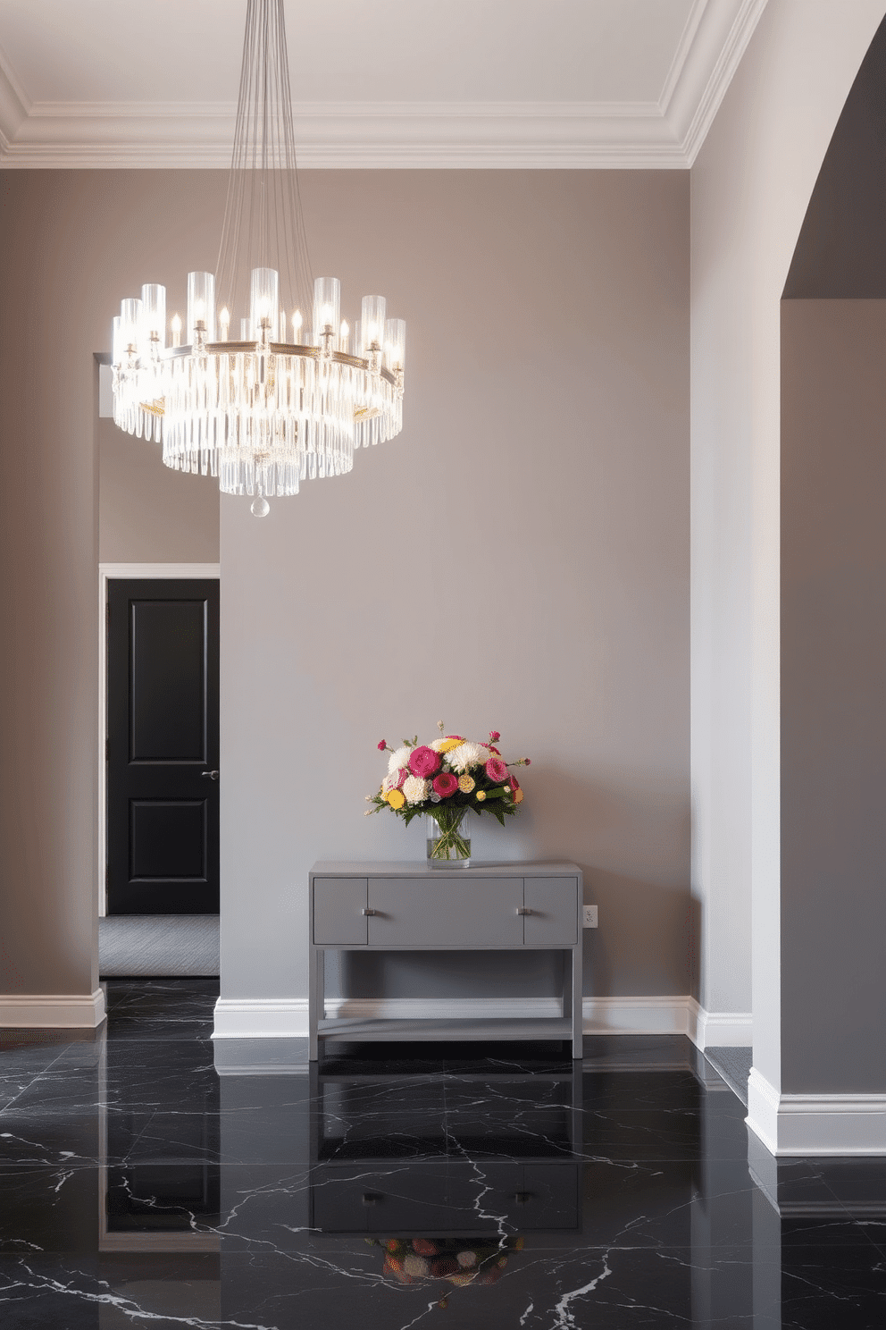 A luxurious foyer featuring a monochromatic color scheme, with walls painted in a soft gray and a sleek, dark marble floor. A stunning chandelier hangs from the ceiling, casting a warm glow over the space, while a minimalist console table in a matching gray tone is adorned with a vibrant bouquet of fresh flowers.