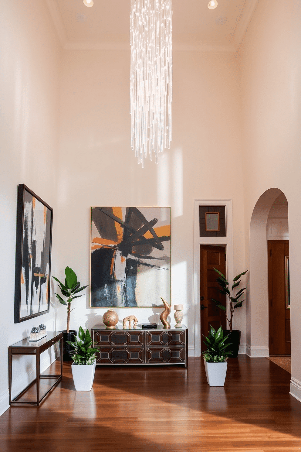 A grand foyer featuring a high ceiling adorned with an elegant chandelier that cascades light throughout the space. Unique art pieces, including a large abstract painting and a sculptural installation, serve as captivating focal points, drawing the eye and enhancing the luxurious atmosphere. The walls are painted in a soft cream hue, complemented by rich hardwood flooring that adds warmth. A stylish console table sits against one wall, topped with decorative objects and flanked by lush greenery in modern planters.