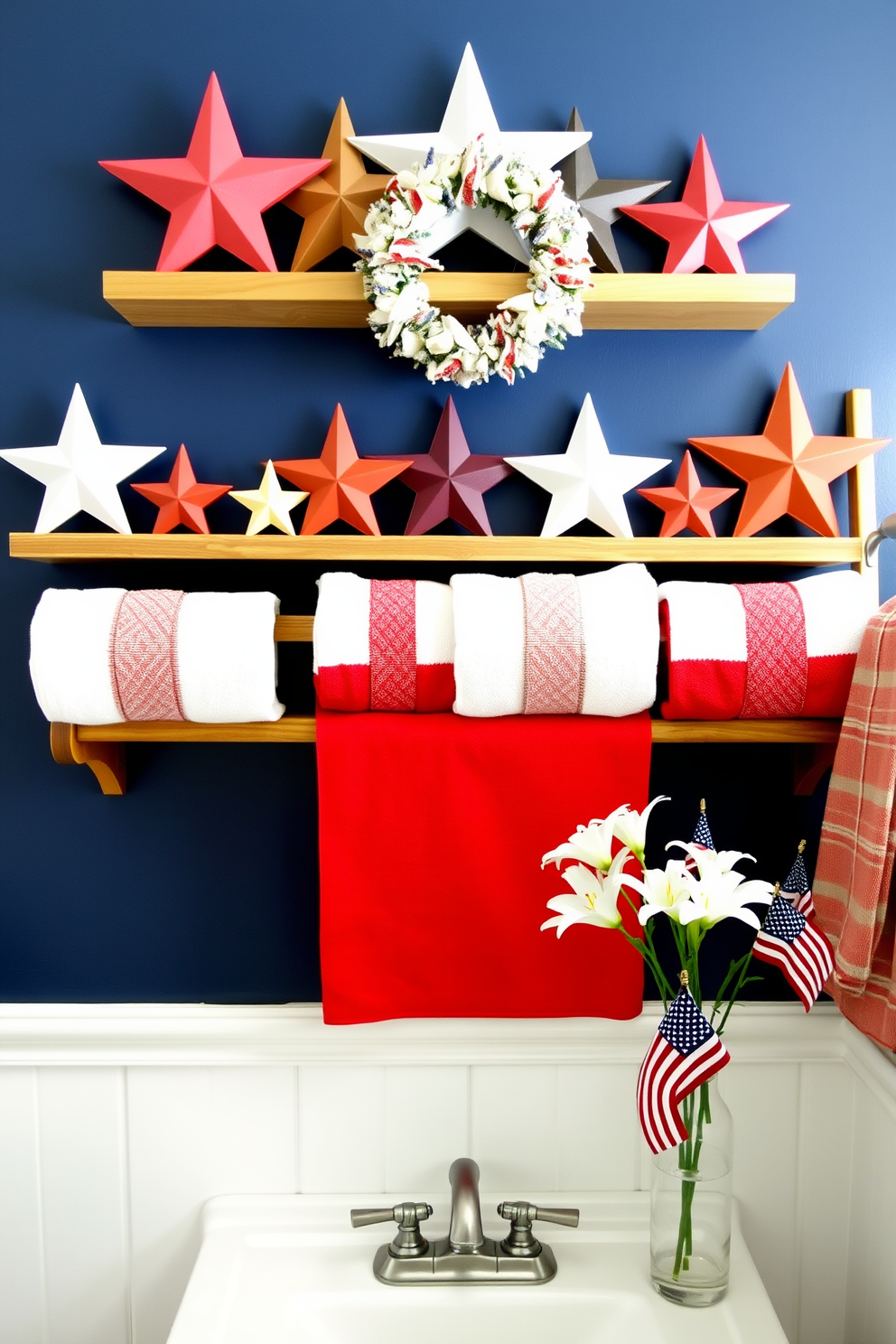 Decorative wooden stars are neatly arranged on floating shelves, with each star varying in size and finish to create visual interest. The shelves are mounted on a backdrop of a navy blue accent wall, providing a striking contrast that highlights the rustic charm of the wooden stars. Memorial Day bathroom decorating ideas feature red, white, and blue towels neatly folded and displayed on a wooden ladder rack. A small, patriotic wreath hangs above the vanity mirror, and a vase filled with fresh white lilies and miniature American flags sits on the countertop, adding a festive touch to the space.