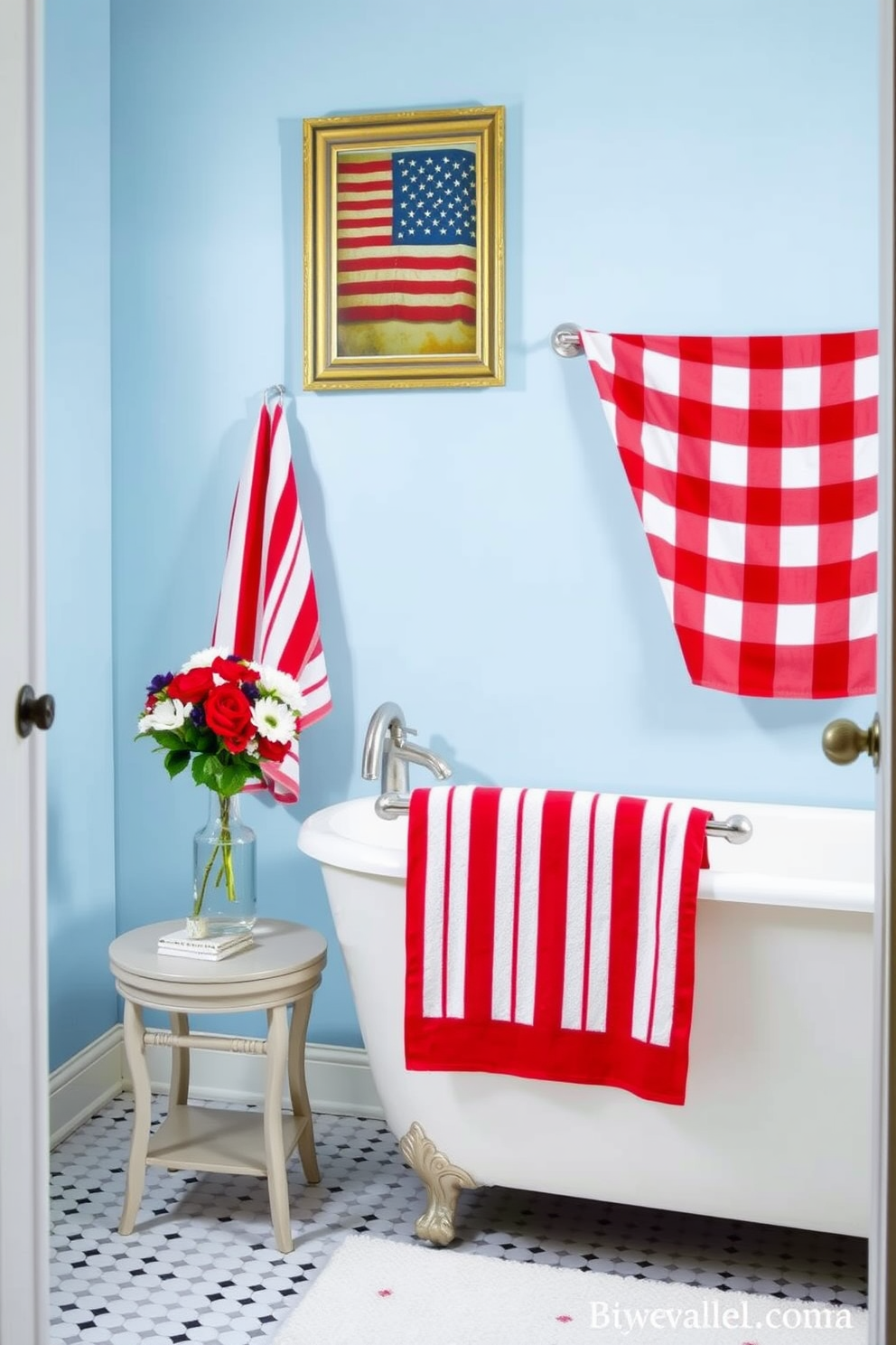 A cozy bathroom with a patriotic theme. Red and white striped bath towels hang neatly on a silver towel rack beside a white porcelain bathtub. The walls are painted in a soft blue shade, reminiscent of the American flag. A small table beside the tub holds a vase with red, white, and blue flowers, and a framed picture of a vintage American flag hangs above the tub.