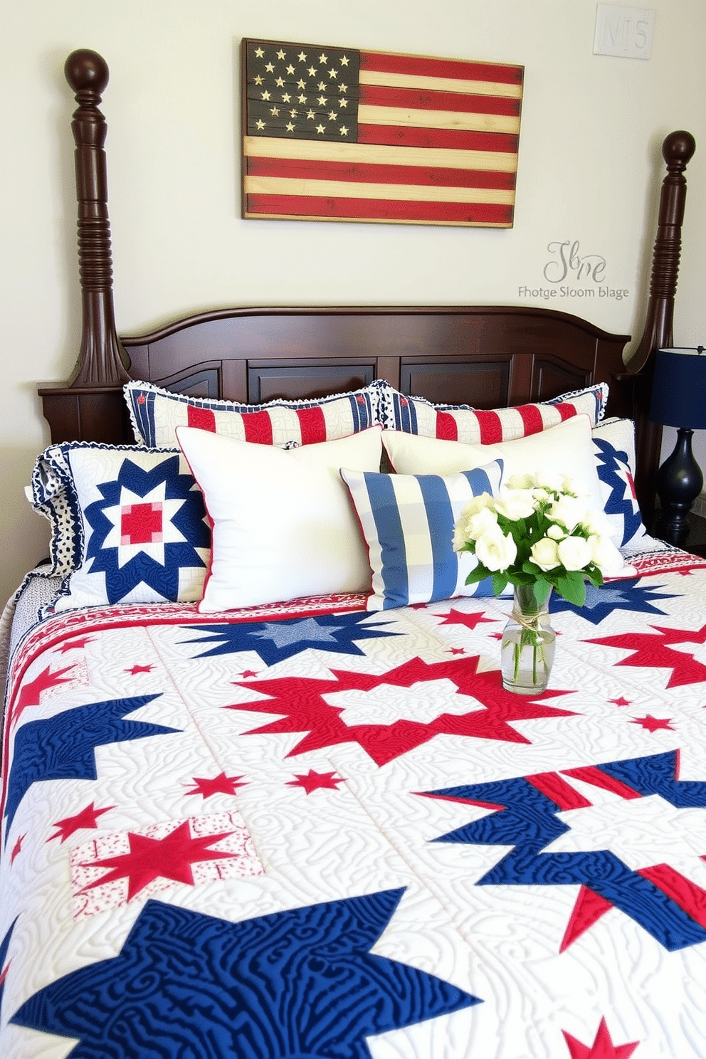 A cozy bedroom adorned with quilted throws featuring patriotic motifs. The bed is covered with a quilt showcasing stars and stripes in red, white, and blue, while matching pillows add to the festive theme. Above the headboard, a wooden plaque with a rustic American flag design hangs, complementing the room's patriotic decor. On the nightstand, a small lamp with a navy blue shade sits next to a vase filled with fresh white flowers, adding a touch of elegance to the Memorial Day celebration.