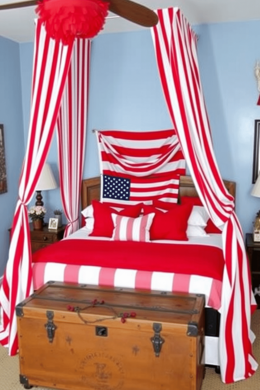 A cozy bedroom decorated for Memorial Day. The bed is adorned with red and white striped curtains as a canopy, creating a patriotic and festive atmosphere. The walls are painted a soft blue, complementing the red and white accents throughout the room. A large American flag hangs above the headboard, and the bed is dressed in white linens with red throw pillows. A vintage wooden trunk at the foot of the bed serves as a storage space and adds a rustic touch.