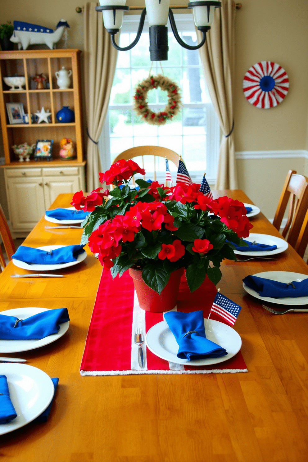 A dining room decorated for Memorial Day, featuring a large wooden table set for a festive meal. Potted red geraniums are placed as the centerpiece, adding a vibrant pop of color to the setting. The table is adorned with a patriotic-themed table runner in red, white, and blue. Surrounding the geraniums, place white dinner plates, blue napkins, and silver cutlery, with additional small American flags as decorative accents.