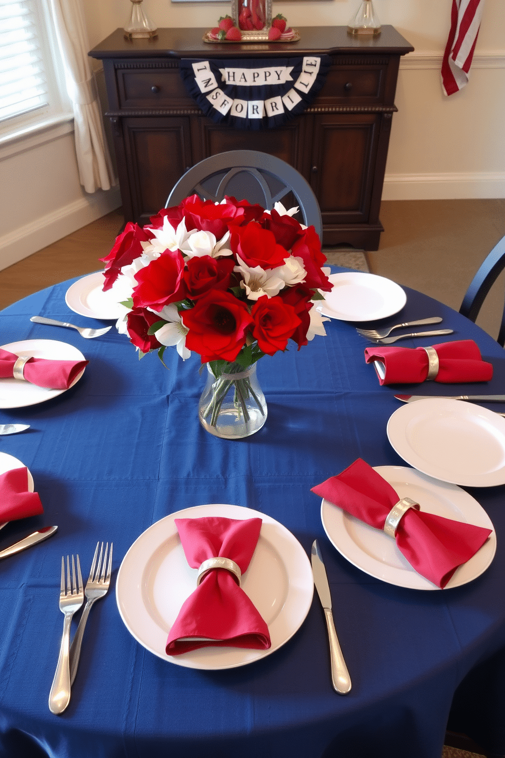 A dining room set for Memorial Day celebrations. The table is covered with an indigo blue tablecloth, adorned with pristine white dishes arranged neatly. Red and white flowers in a clear glass vase serve as the centerpiece, adding a touch of elegance. Patriotic-themed napkins are folded beside each plate, and silver cutlery gleams under the soft lighting.