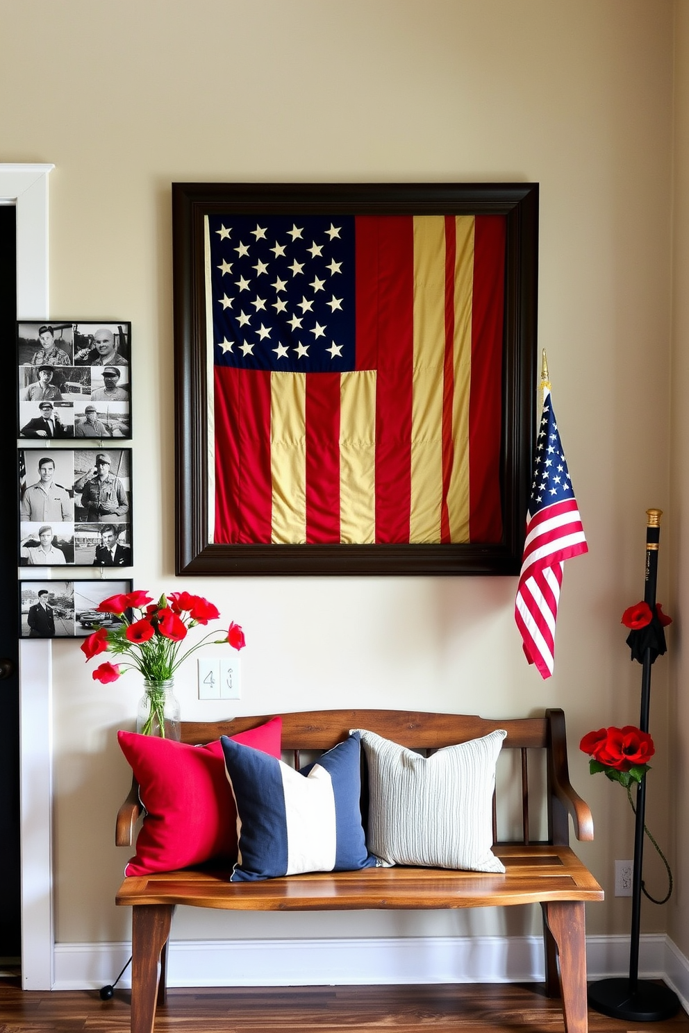 An entryway dedicated to Memorial Day, featuring a vintage flag display on the wall. The flag is carefully framed in a dark wooden frame, and beneath it, a rustic wooden bench is adorned with red, white, and blue throw pillows. On the wall adjacent to the flag, a series of black-and-white photographs of military servicemen and women are arranged in a grid pattern. A small table next to the bench holds a vase filled with red poppies, and an American flag stands proudly in a corner umbrella stand.