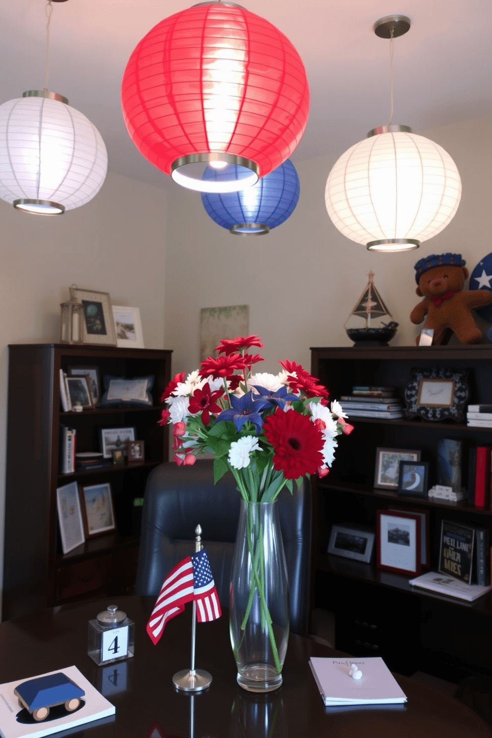 A home office decorated for Memorial Day featuring red white and blue paper lanterns hanging from the ceiling. The desk is adorned with patriotic themed accessories including a small flag and a vibrant floral arrangement in a glass vase.