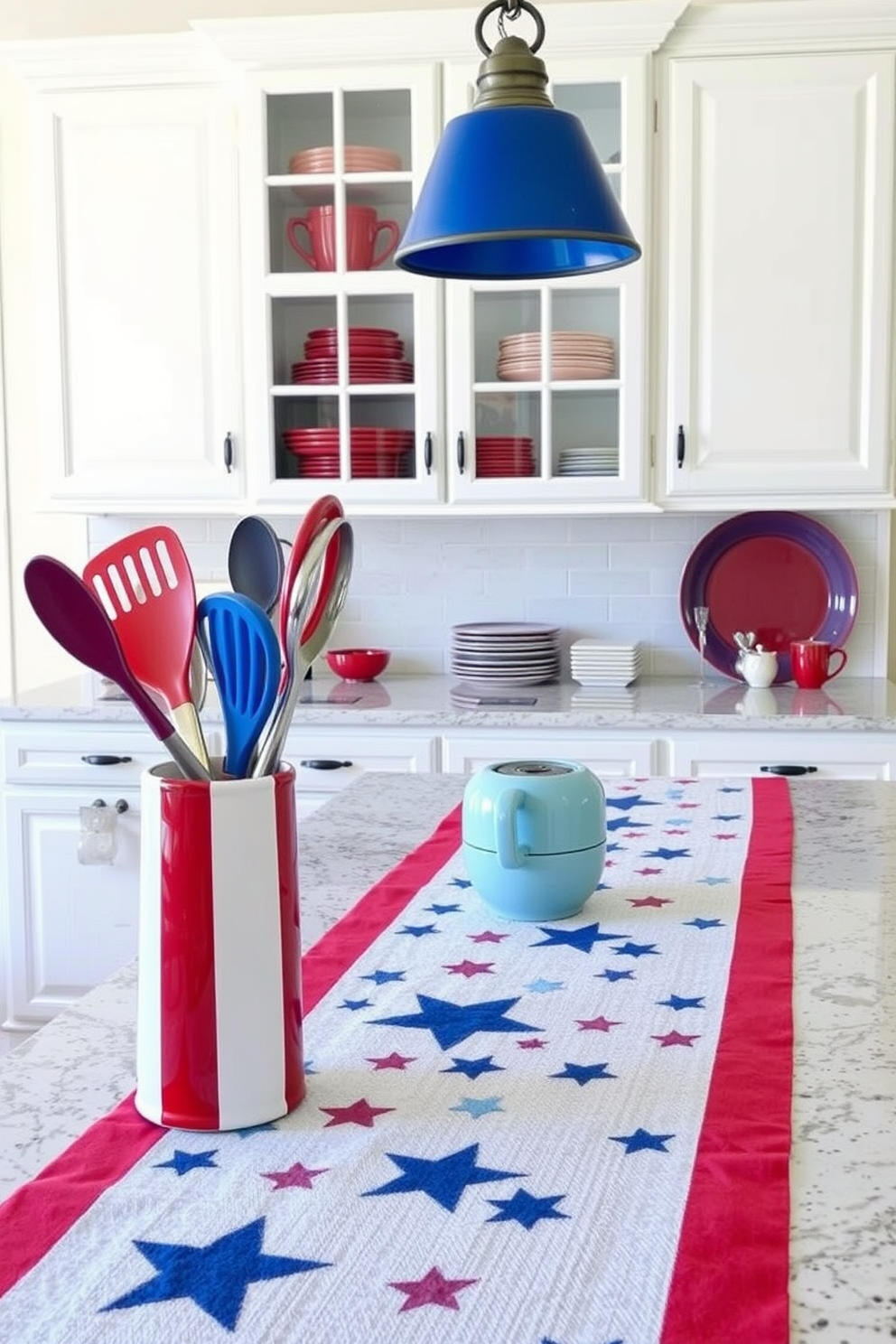 A Memorial Day-themed kitchen setting. On the countertop, a red, white, and blue utensil holder stands prominently, holding various kitchen tools. The kitchen island is decorated with a patriotic table runner, featuring stars and stripes. Hanging above the island, pendant lights with blue shades cast a warm glow. In the background, a white cabinet displays red and blue dishware, creating a cohesive and festive look.