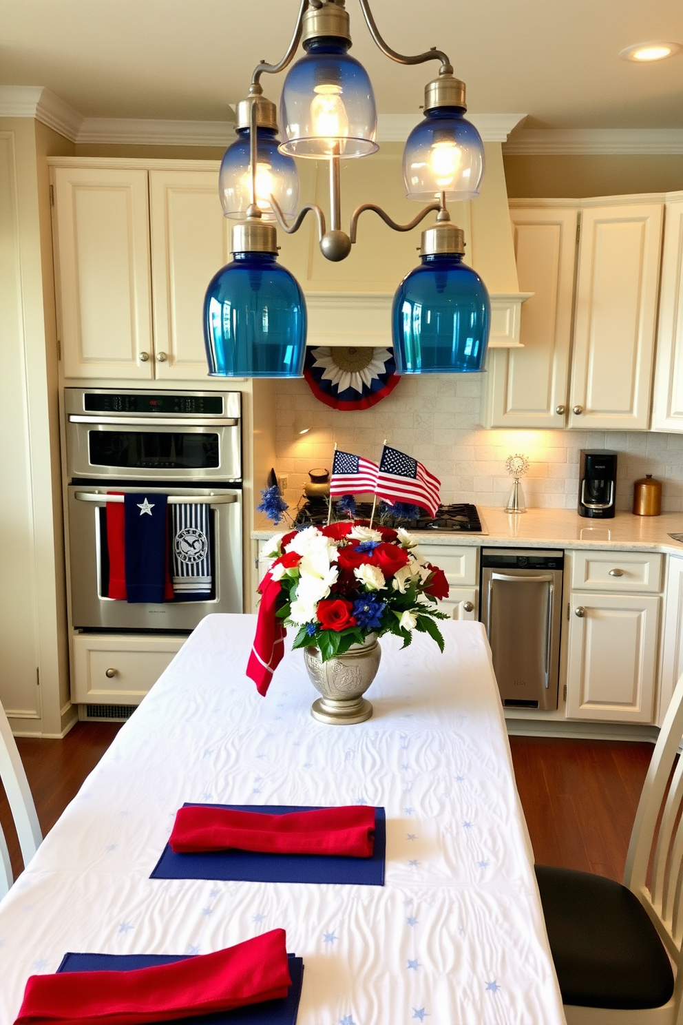 A cozy kitchen decorated for Memorial Day. Red and blue dish towels hang from the oven handle, adding a patriotic touch. The kitchen island is adorned with a centerpiece featuring a blend of red, white, and blue flowers. Above the island, pendant lights with blue glass shades cast a warm glow. A white tablecloth with subtle star patterns covers the dining table, complemented by red and blue napkins.