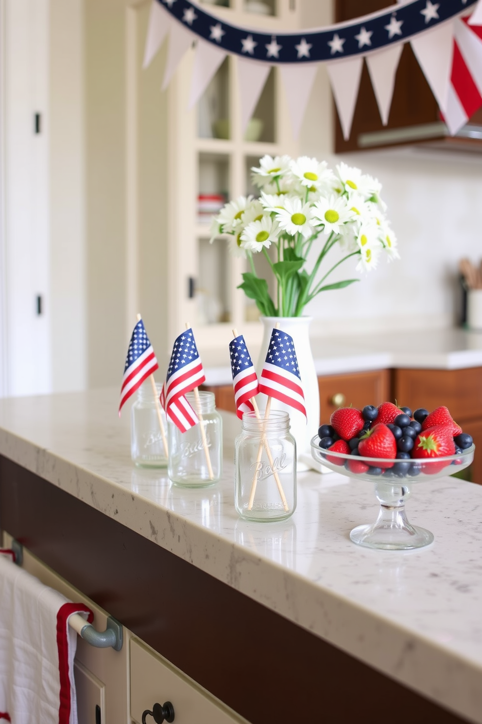 A cozy kitchen adorned for Memorial Day celebrations. On the countertop, decorative mason jars filled with miniature American flags stand proudly, adding a patriotic touch. The jars are arranged next to a bowl of fresh strawberries and blueberries, enhancing the festive red, white, and blue theme. Above the counter, a banner with stars and stripes hangs, while a vase of white daisies completes the charming holiday look.