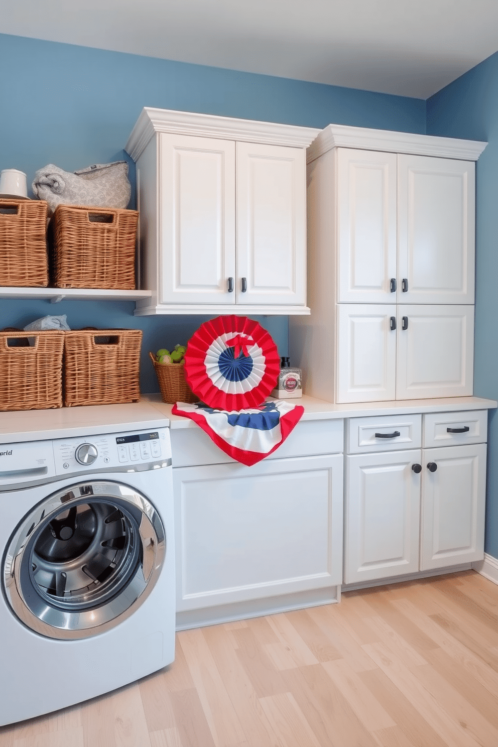 A bright and airy laundry room featuring wicker baskets for storage. The walls are painted in soft blue, complemented by white cabinetry and a spacious countertop for folding clothes. On the floor, there is a durable, light-colored vinyl that mimics wood. A cheerful arrangement of red, white, and blue decor elements celebrates Memorial Day, adding a festive touch to the space.