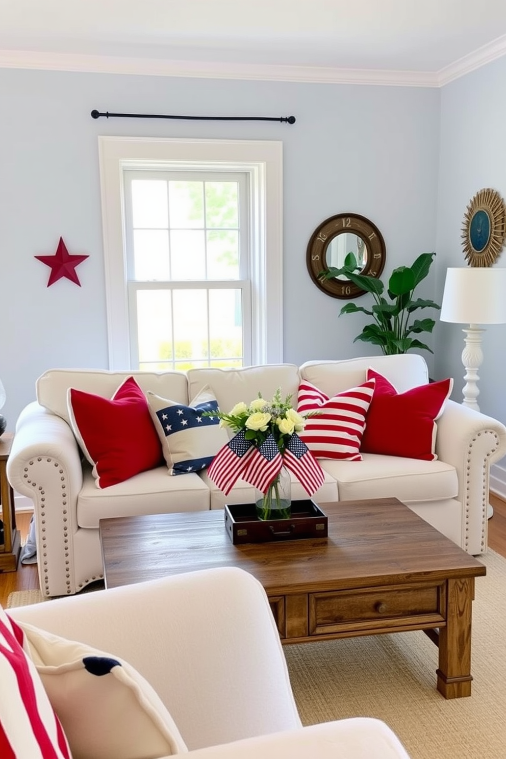 A cozy living room adorned with red, white, and blue throw pillows. The pillows are arranged on a plush white sofa, creating a patriotic theme perfect for Memorial Day. A rustic coffee table sits in front of the sofa, decorated with a vase of fresh flowers and small American flags. The room features light blue walls and hardwood floors, with a large window letting in natural light and a gentle breeze.