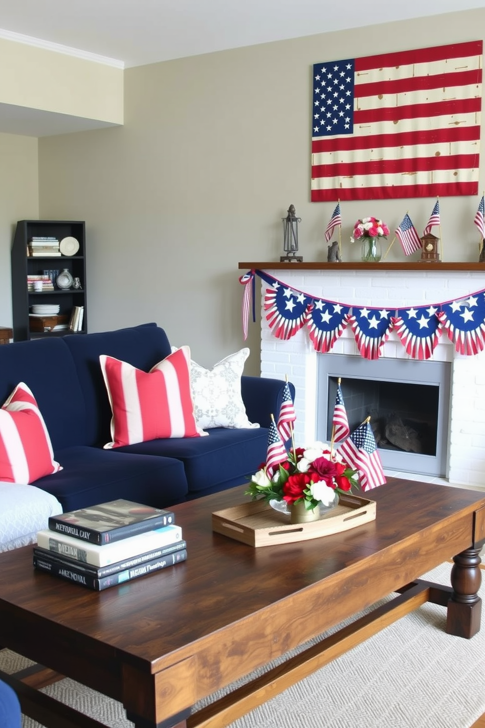 A cozy living room decorated for Memorial Day. The space features a navy blue sofa adorned with red and white throw pillows, and a rustic wooden coffee table displaying patriotic-themed coffee table books, including titles on American history and national parks. On the wall behind the sofa, a large American flag art piece hangs, complemented by red, white, and blue bunting draped across the mantel of a white brick fireplace. The room is accented with small American flags in decorative vases and a centerpiece of red, white, and blue flowers on the coffee table.