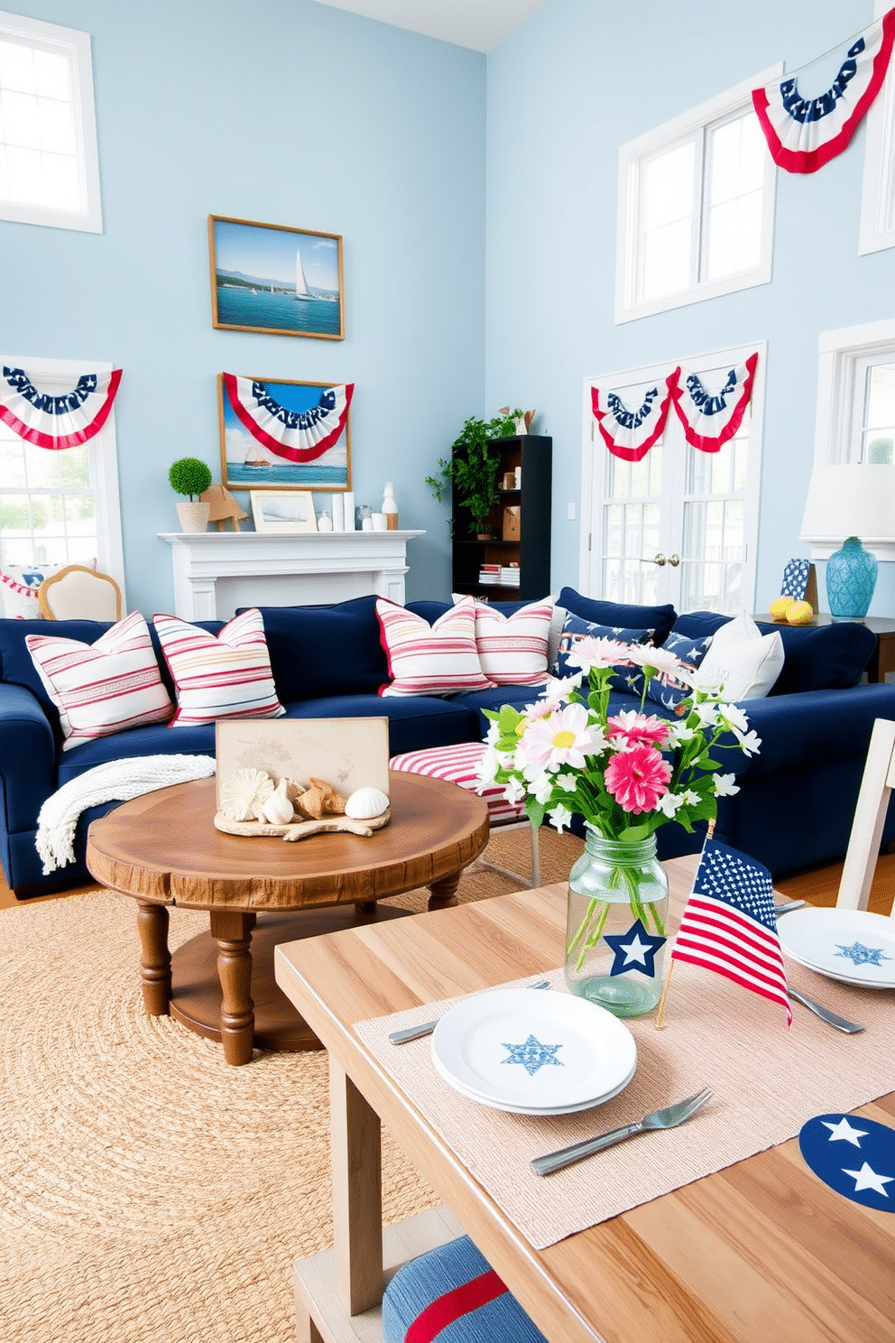 A bright and airy living space inspired by nautical themes. The room features a navy blue sectional sofa adorned with white and red striped throw pillows, and a large round jute rug anchors the seating area. Decorative elements include a collection of seashells and driftwood art displayed on a rustic wooden coffee table. The walls are painted in a soft sky blue, and nautical-themed artwork hangs above the mantel, creating a perfect summer vibe. For Memorial Day, the loft is decorated with patriotic accents. Red, white, and blue bunting drapes across the windows, and a festive table setting showcases star-patterned tableware alongside fresh flowers in a mason jar.