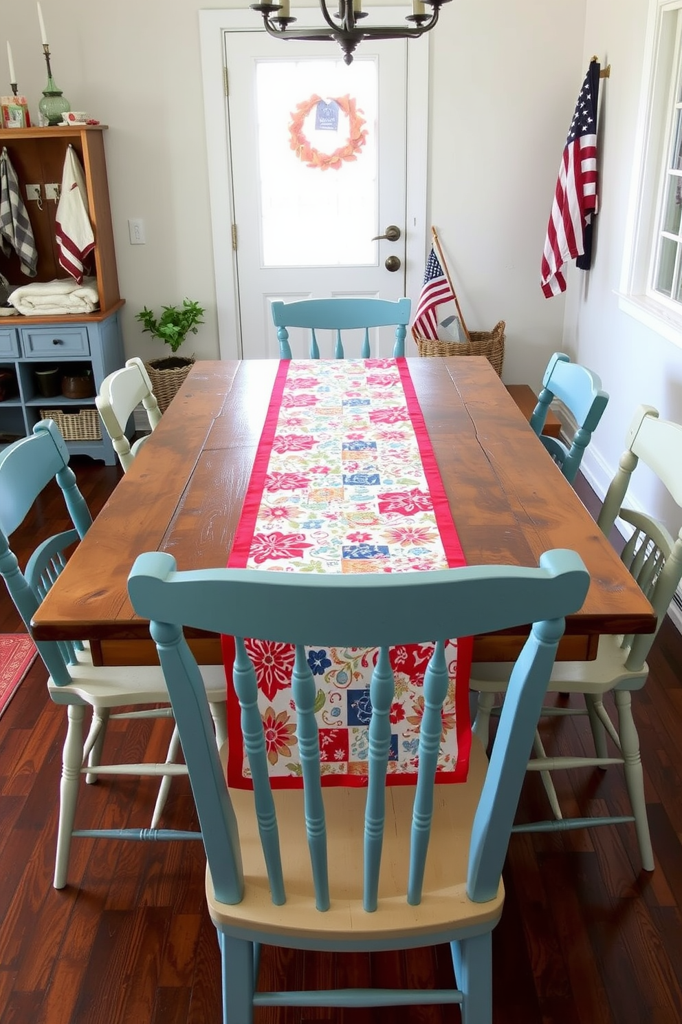 A seasonal table runner adorned with festive patterns stretches elegantly across a rustic wooden dining table. Surrounding the table are mismatched chairs, each painted in vibrant colors that complement the cheerful design of the runner. For Memorial Day, the mudroom is decorated with red, white, and blue accents that evoke a sense of patriotism. A woven basket filled with blankets and a small flag display add a warm and inviting touch to the space.