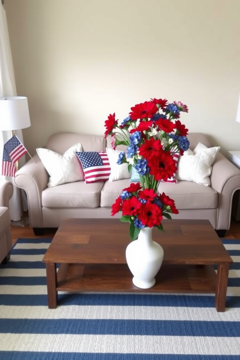 A cozy small living room decorated for Memorial Day. The sofa is adorned with red, white, and blue throw pillows, creating a patriotic theme. A wooden coffee table sits in front of the sofa, topped with a white vase filled with fresh red and blue flowers. The walls are painted a soft beige, and a blue and white striped rug adds to the festive atmosphere.