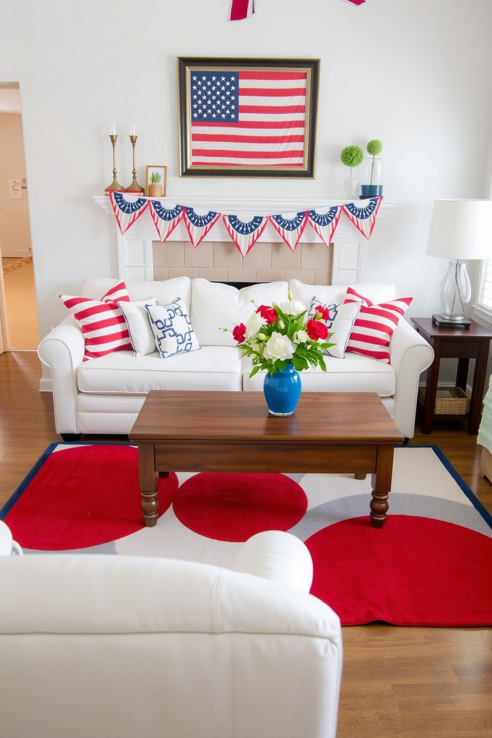 A cozy small living room decorated for Memorial Day. A red, white, and blue area rug anchors the space, complemented by a white sofa adorned with patriotic-themed throw pillows. A wooden coffee table sits atop the rug, showcasing a centerpiece of fresh flowers in a blue vase. Red and white bunting hangs from the mantel, and a framed American flag is displayed on the wall above.