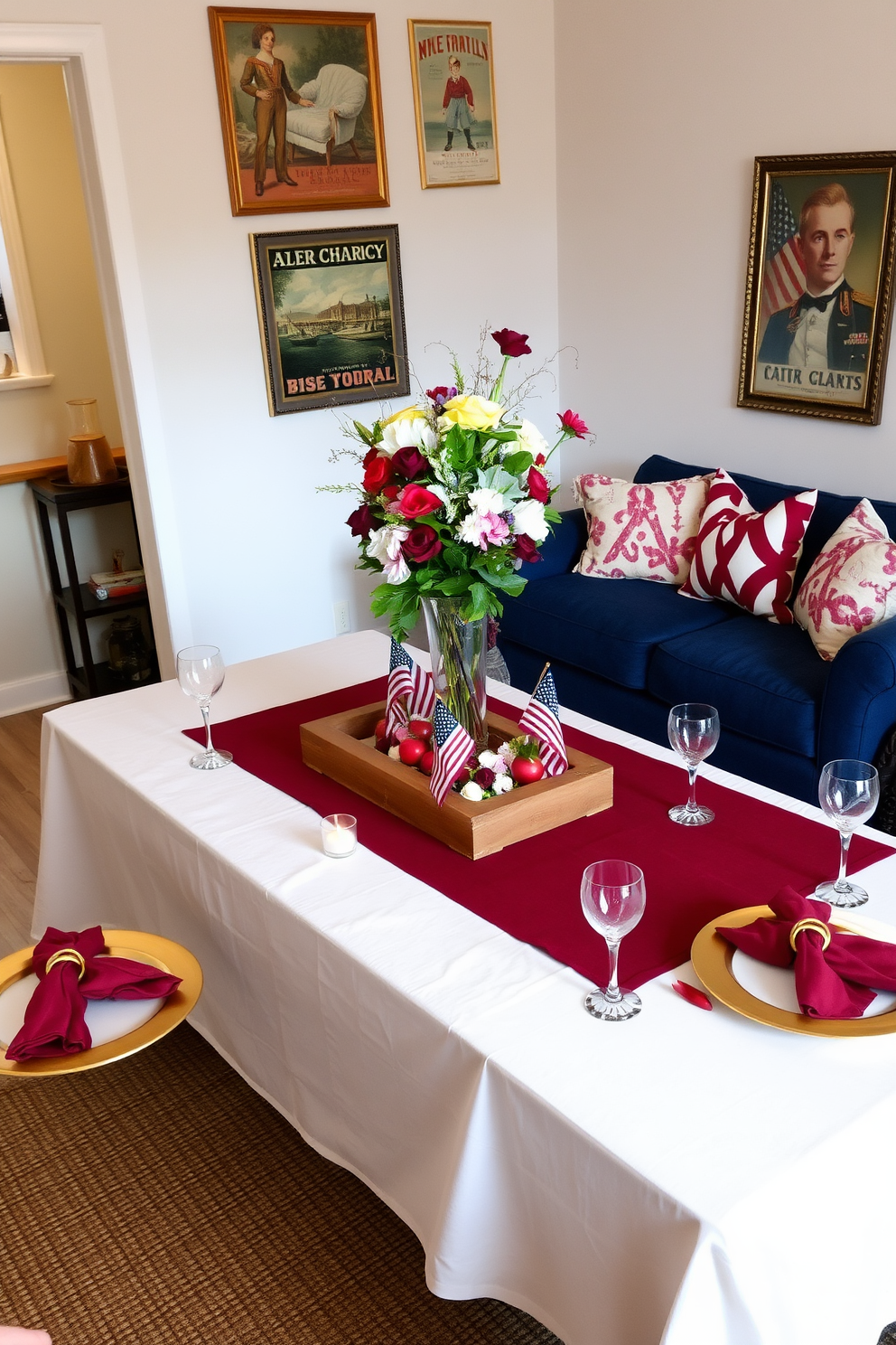 A festive table setting for gatherings. The table is adorned with a crisp white tablecloth, overlaid with a rich burgundy runner. At each place setting, there are gold-rimmed plates, crystal glassware, and silver cutlery, accented by deep red napkins tied with elegant gold rings. The centerpiece is a lush arrangement of seasonal flowers in a tall glass vase, surrounded by small, flickering tea lights. Memorial Day small living room decorating ideas. The room features a cozy seating area with a navy blue loveseat, complemented by red and white throw pillows. A rustic wooden coffee table sits in the center, decorated with a patriotic-themed centerpiece, including miniature American flags and fresh flowers. The walls are adorned with framed vintage posters, and a woven rug in red, white, and blue hues anchors the space.