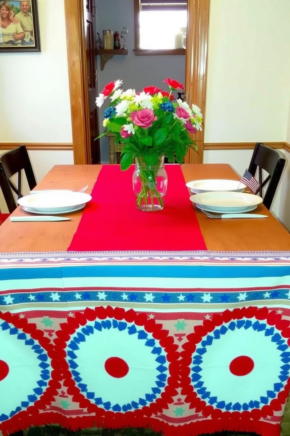 A vibrant dining table is adorned with a red, white, and blue table runner that creates a festive atmosphere. The runner is complemented by simple white dinnerware and fresh flowers in a glass vase, evoking a sense of celebration. In a cozy small space, the table is set against a backdrop of light-colored walls and wooden accents. Decorative elements like star-shaped candles and small flags add a patriotic touch to the overall decor.