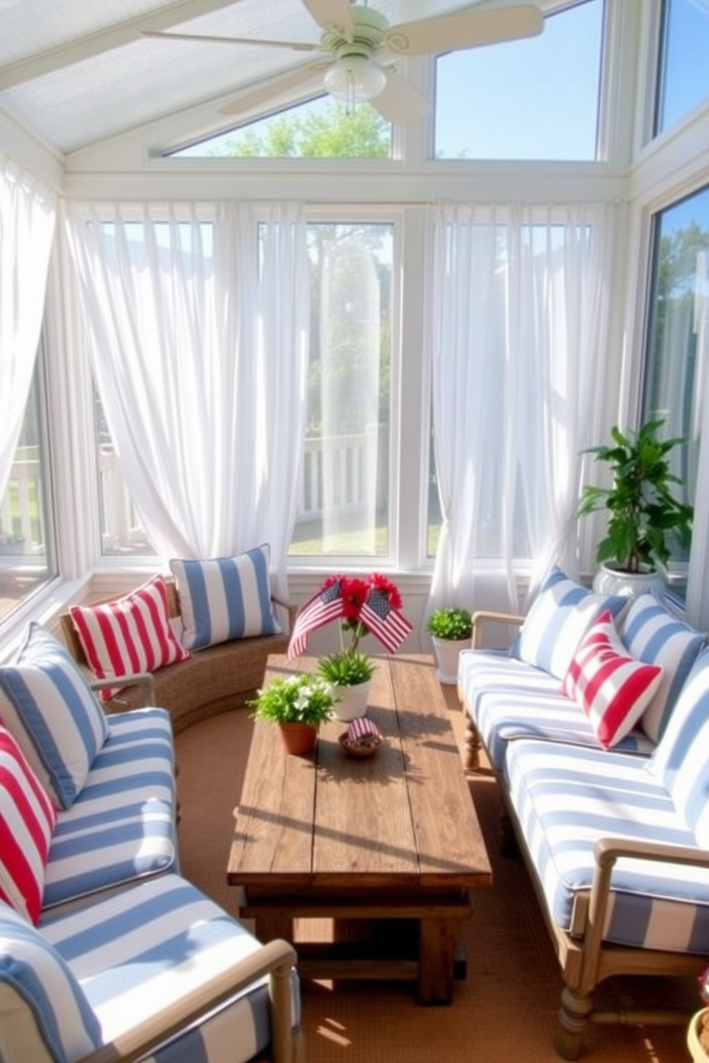 A bright and airy sunroom features a cozy seating arrangement with striped cushions in shades of blue and white. Large windows allow natural light to flood the space, adorned with sheer white curtains that flutter gently in the breeze. A rustic wooden coffee table sits at the center, surrounded by potted plants that bring a touch of nature indoors. Festive patriotic decor, such as small flags and red, white, and blue accents, add a cheerful touch for Memorial Day celebrations.