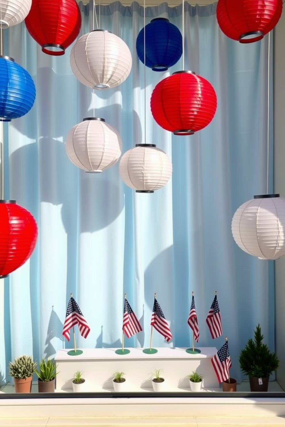 A festive window display featuring paper lanterns in vibrant red, white, and blue hues. The lanterns are suspended at varying heights, creating a playful and patriotic atmosphere. Beneath the lanterns, a white window sill is adorned with small potted plants and American flags. The backdrop is a light blue curtain that enhances the holiday spirit and complements the colors of the lanterns.