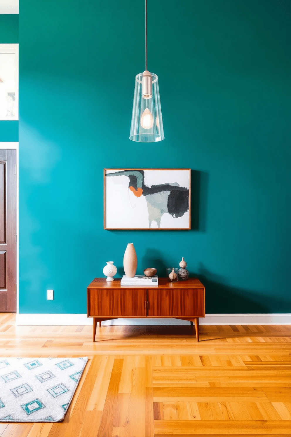 A striking foyer features an accent wall painted in a bold, deep teal, creating a dramatic backdrop for the space. Flanking the entrance are two sleek Mid Century Modern console tables, showcasing geometric shapes and rich wood finishes. The floor is adorned with a warm, honey-toned hardwood, complementing the vibrant wall color. A stylish pendant light hangs from the ceiling, casting a soft glow over a curated selection of decorative objects and a large, abstract art piece.