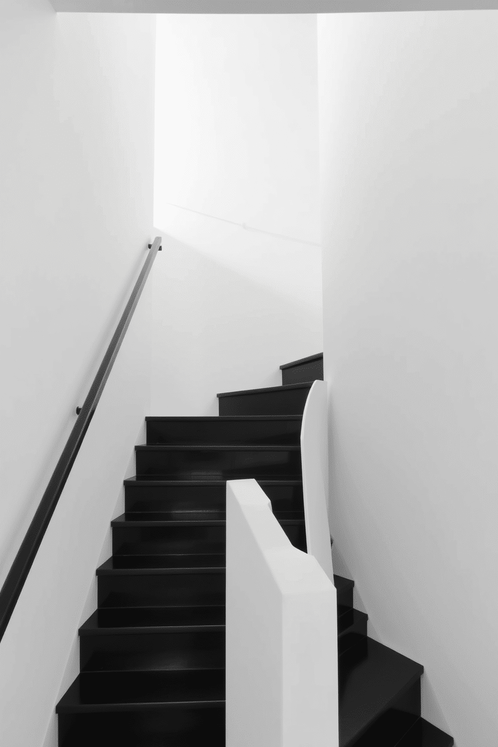 A minimalist black staircase ascends gracefully, featuring clean lines and a sleek handrail that complements its modern aesthetic. The surrounding walls are painted white, enhancing the staircase's bold contrast and creating a sense of openness and lightness in the space.