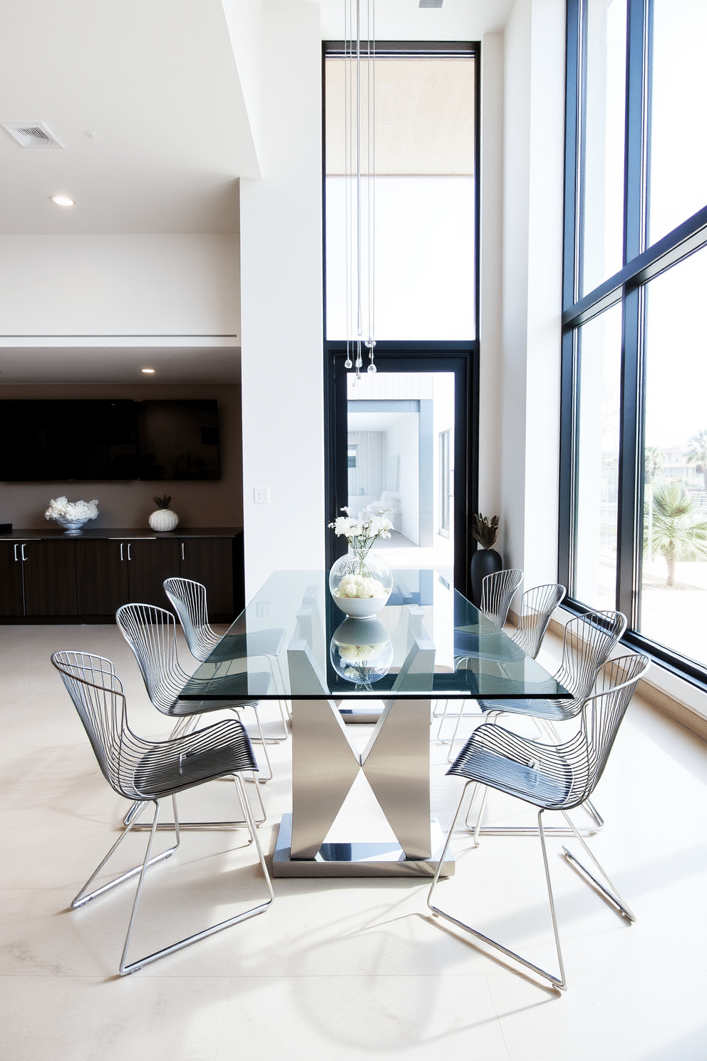 A sleek glass dining table is set in the center of a modern dining room, surrounded by elegant metal chairs featuring minimalist designs. Large windows allow natural light to flood the space, highlighting the clean lines and contemporary decor.