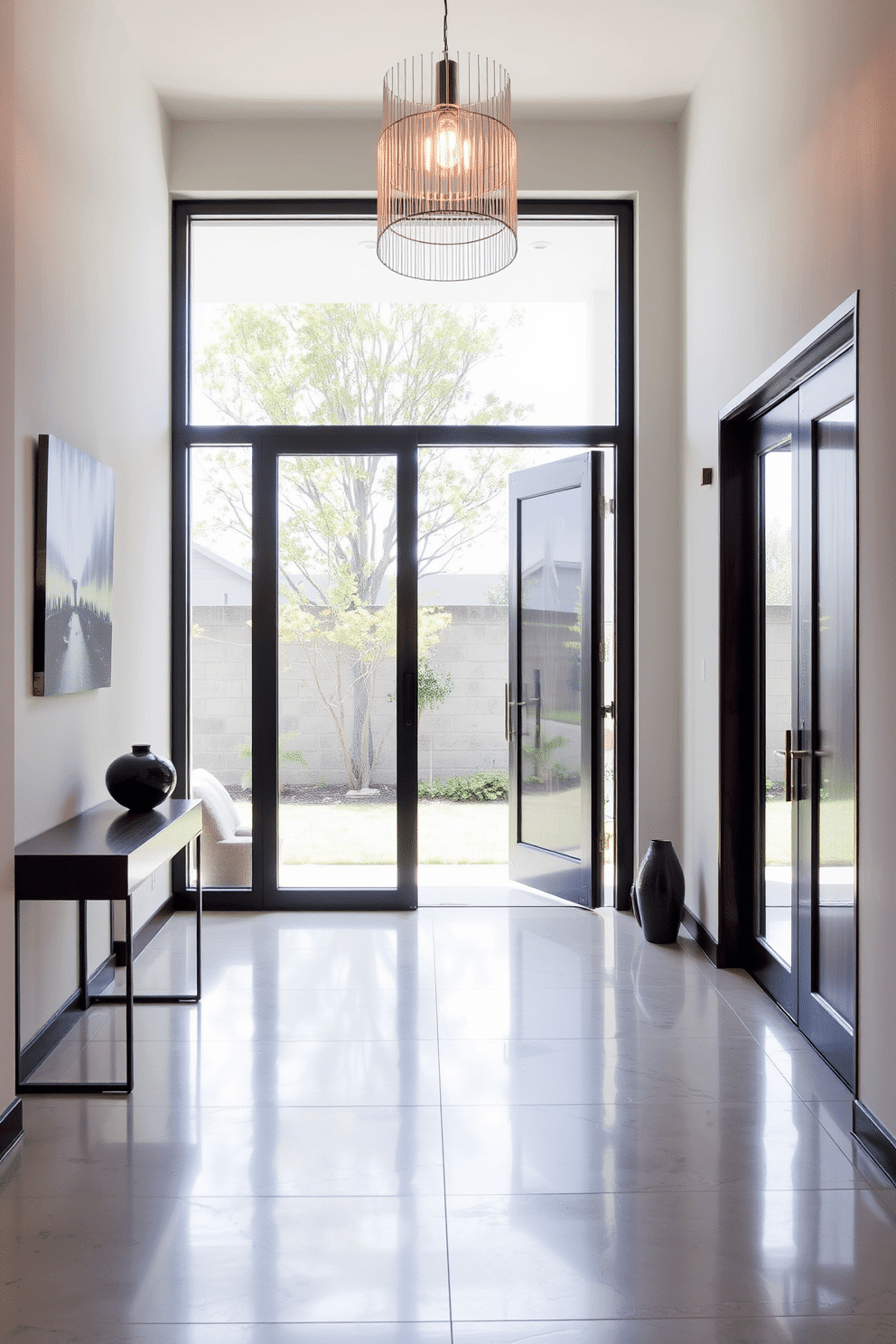 A modern foyer featuring a glass entry door that allows natural light to flood the space. The floor is adorned with sleek, large-format tiles, and a minimalist console table sits against one wall, complemented by a statement pendant light above.