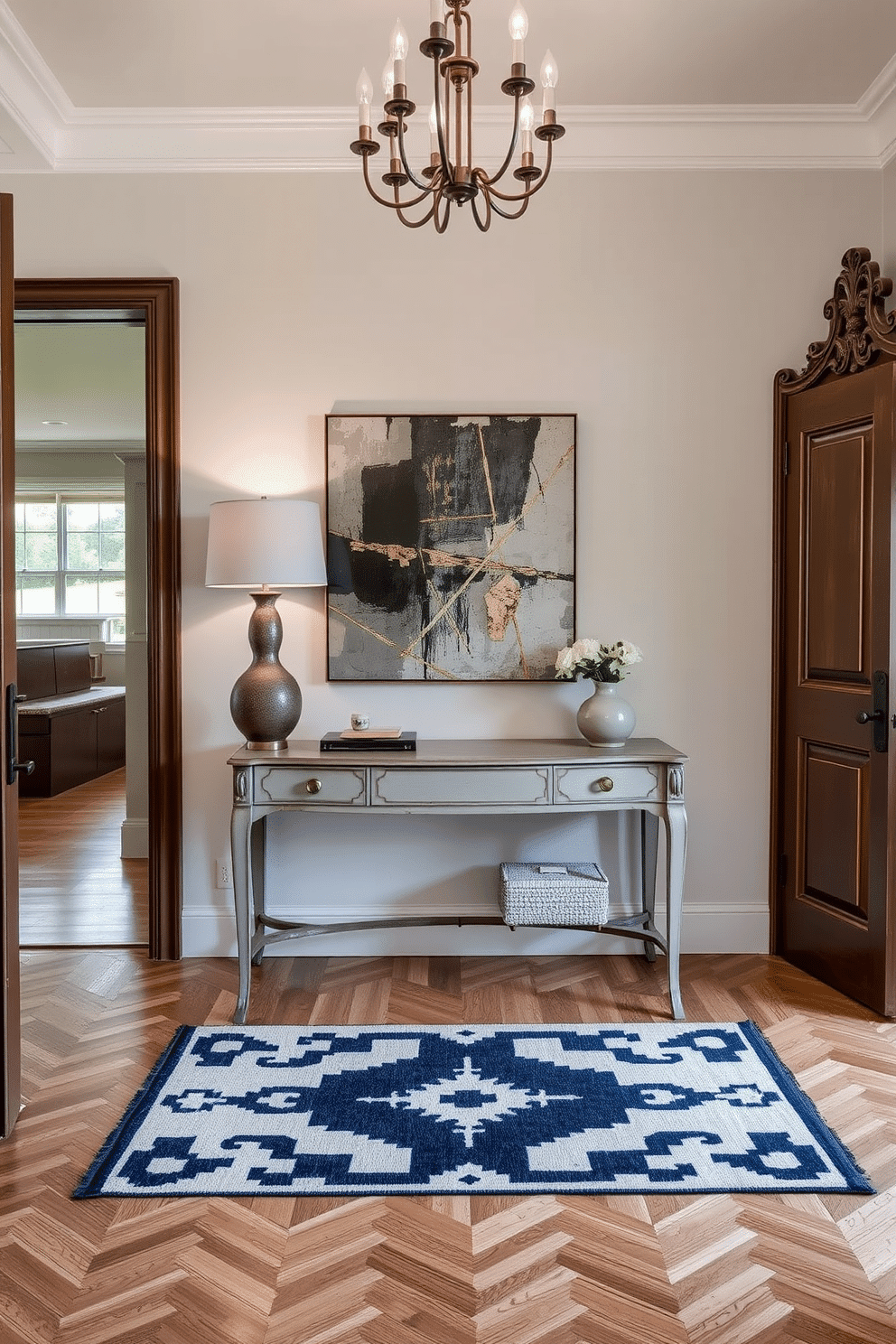 A stylish foyer that seamlessly blends vintage accents with modern elements. The space features a sleek console table with a distressed finish, adorned with a contemporary lamp and a large abstract artwork above it. On the floor, a geometric patterned rug contrasts beautifully with the classic herringbone wood flooring. A vintage mirror with an ornate frame hangs on the wall, reflecting light from a modern chandelier overhead.